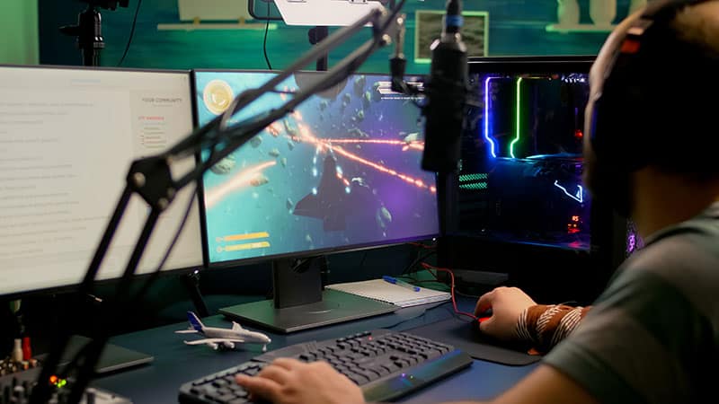 Back view of a gaming streamer with two monitors, microphone and headphones.