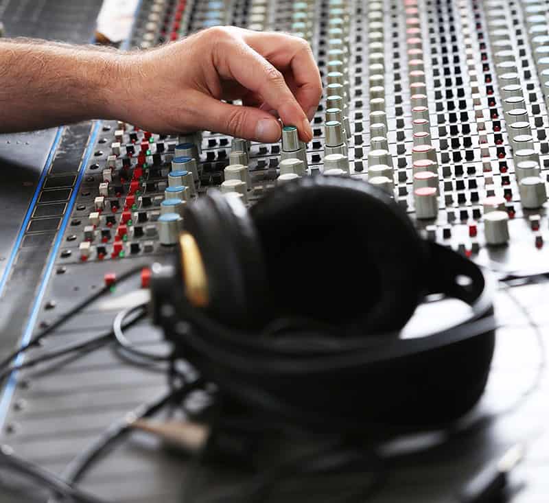 Headphones sitting on a mixing console with a man adjusting a knob.