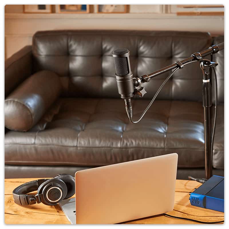 Audio-Technica AT2020 on a stand with a laptop and headphones in the foreground.