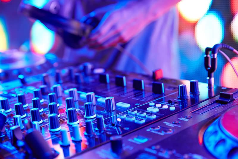 Close up photo of DJ gear with a DJ picking up a pair of headphones in the background