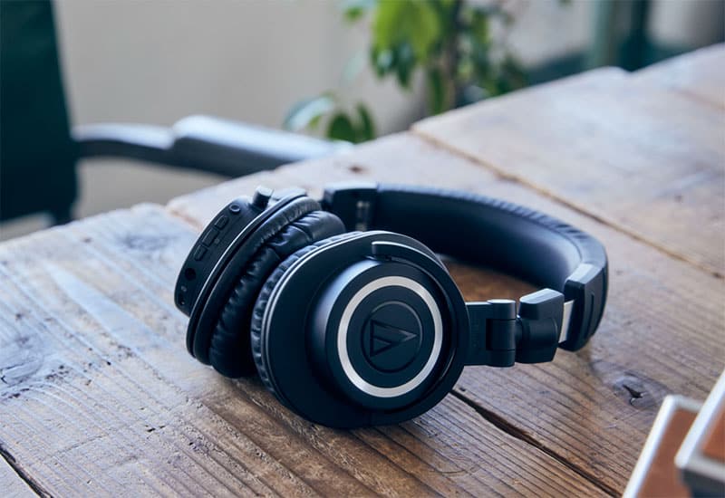 Audio-Technica ATH-M50xBT2 headphones laying on a wooden desk.