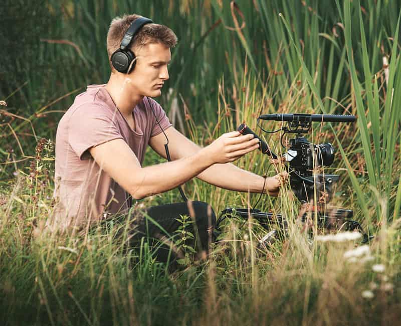 Man in a field with Beyerdynamic DT 240 PRO headphones and video recording equipment.