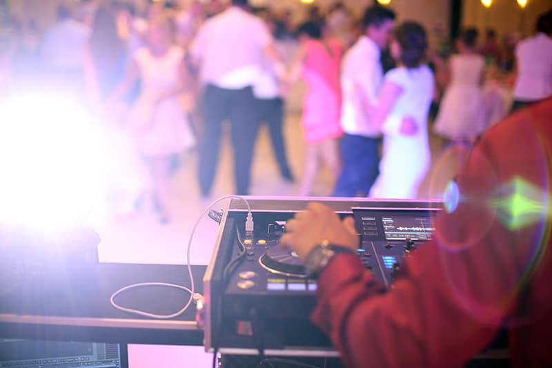 DJ playing at a wedding with dancing couples of the dancefloor.