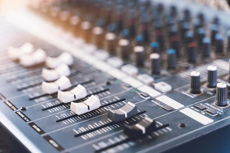 Professional sound mixer with faders and knobs.