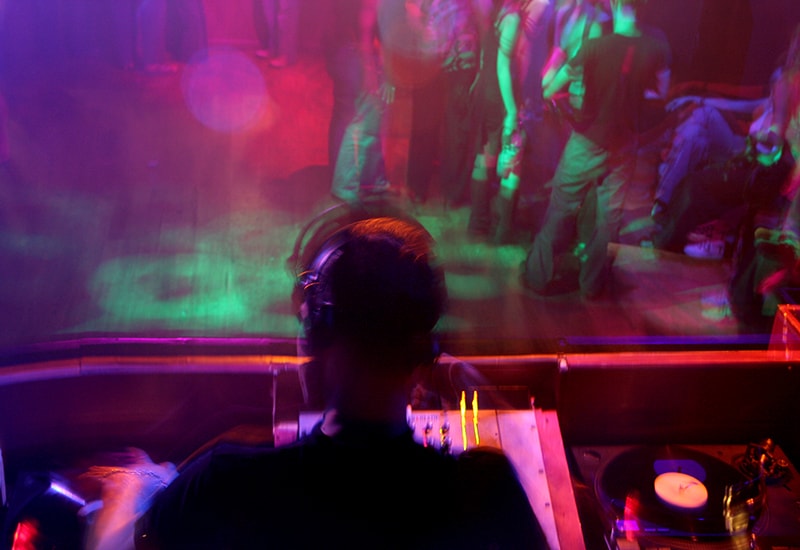 Dj playing in a nightclub with people on the dancefloor.
