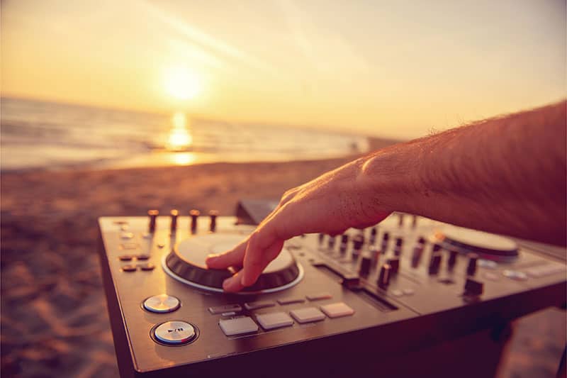 Photo of a DJ using a portable DJ controller at the beach.