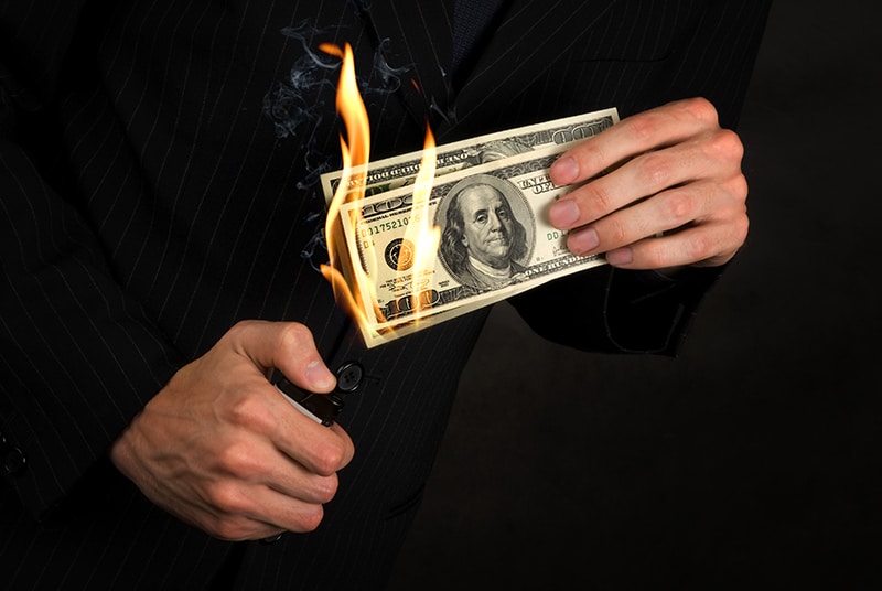 Man in a suit setting fire to money.