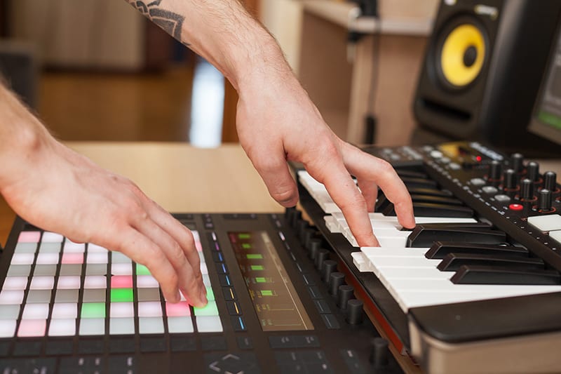 Music producer in a studio using a keyboard and MIDI launchpad.