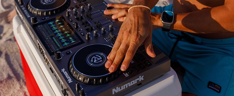 Man using the Numark MIxstream Pro Go on a cooler at the beach.