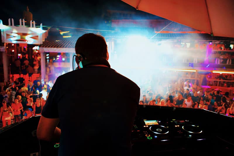 Backlit DJ with headphones performing at a nightclub.