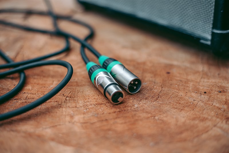Two green XLR cables on a wooden desk next to a speaker.