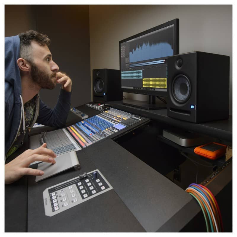 Man sitting at a mixing desk looking at a screen with PreSonus Eris 5 studio monitors on either side of the screen.