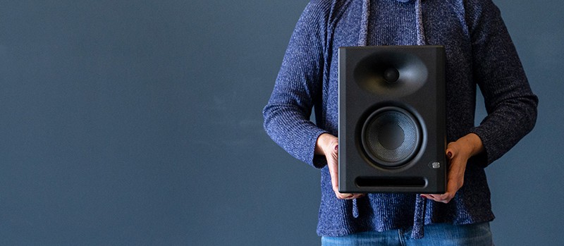 Woman holding a PreSonus Eris E5 XT studio monitor with a blue background.