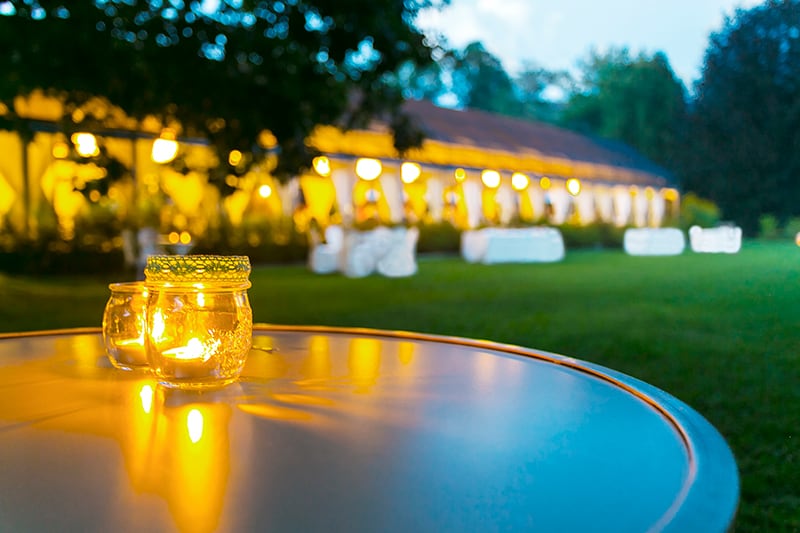 Outdoor table with candles on it with more tables in the background outside of a house.