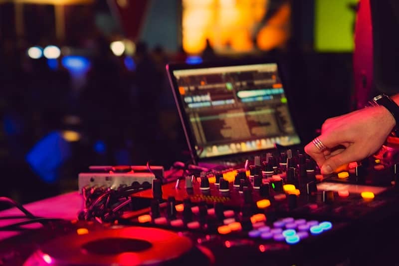DJ performing on DJ equipment with a laptop in the background.