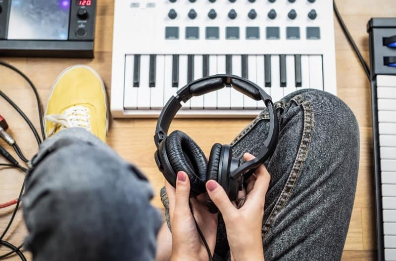Man holding a pair of headphones surrounded by music equipment.