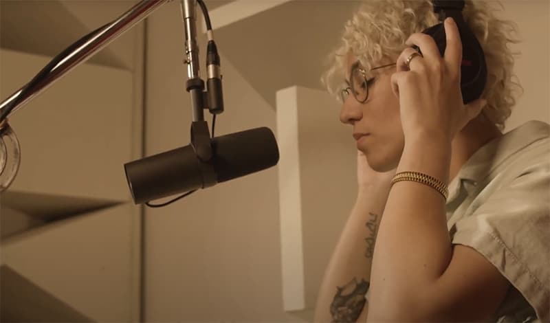 Woman in a recording studio in front of a microphone with headphones on.