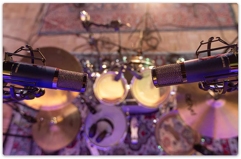 A pair of Telefunken TF11 microphones above a drum kit.