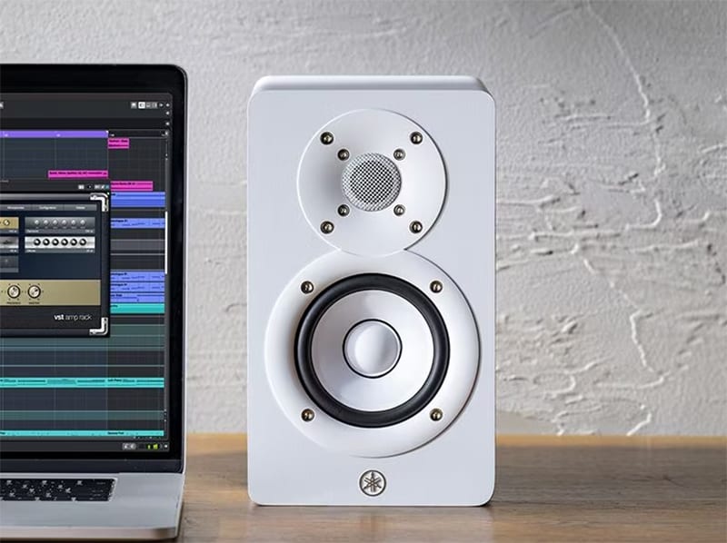White Yamaha HS3 monitor sitting on a desk next to a laptop.