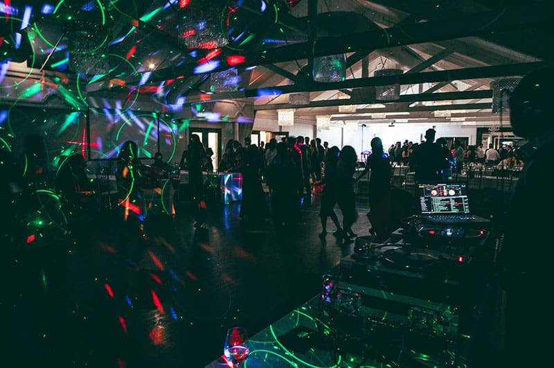 A DJ playing at a nightclub with disco lights and people dancing.