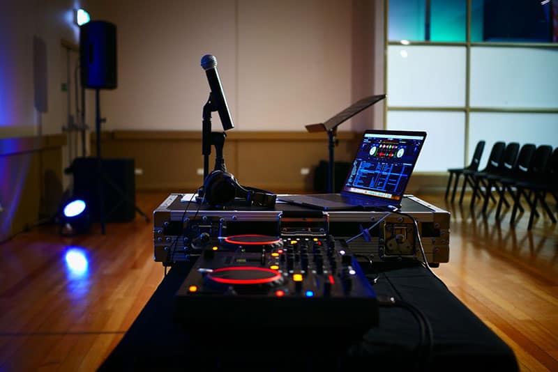 Photo of a DJ setup in a hall with lights and speakers in the background