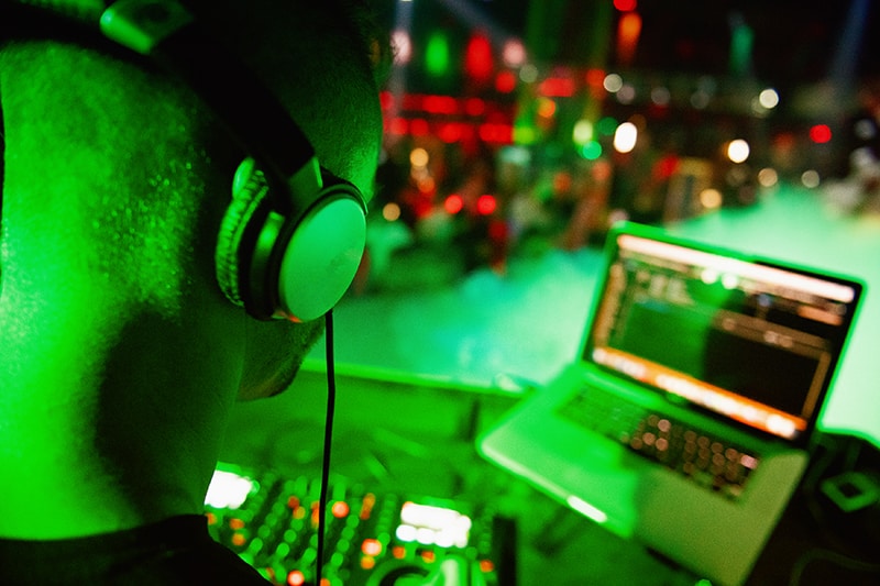 DJ using a DJ mixer and laptop in a nightclub.