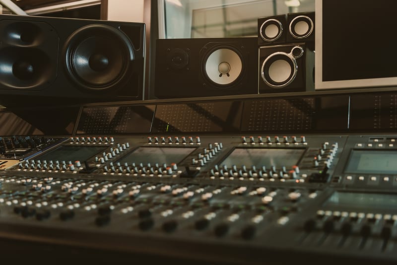 Mixing desk with various studio monitors on a shelf.