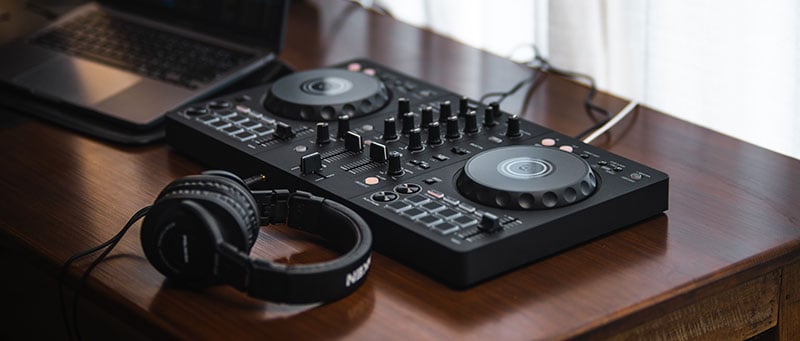 DJ controller, laptop, and headphones on a desk.