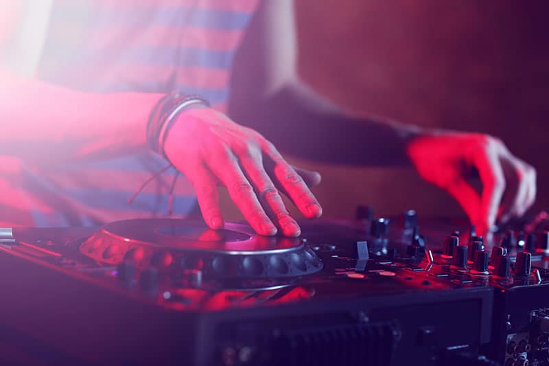 DJ using a jog wheel and manipulating EQ controls on DJ equipment.