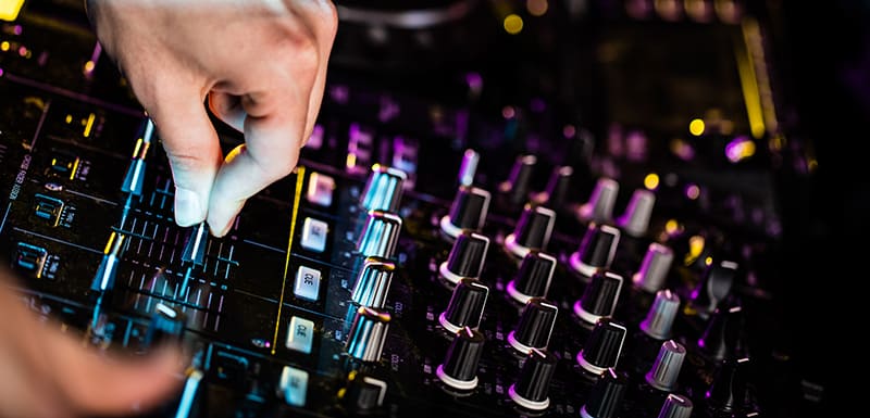 Close up photo of a DJ mixer with a DJ using the faders.