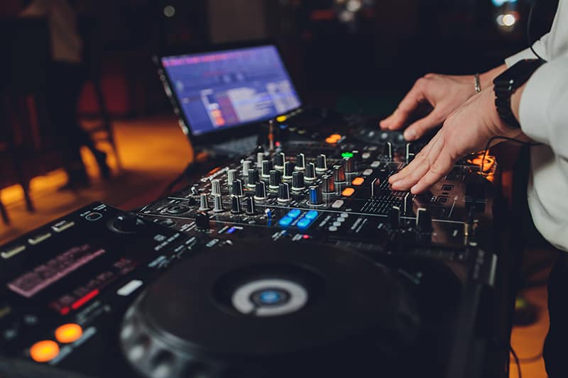 DJ using DJ equipment with a laptop in the background.