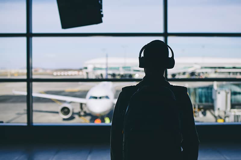 Back of a man with headphones on at an airport looking at a plane.