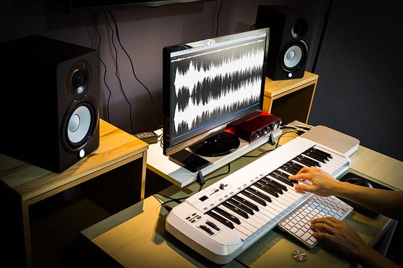 Studio Monitors sitting next to a computer screen with a MIDI keyboard in front